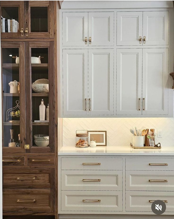 a kitchen with wooden cabinets and white counter tops in front of a glass fronted bookcase