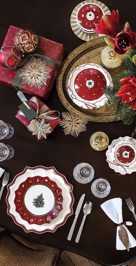 the table is set for christmas dinner with red and white plates, silverware, and gifts