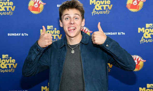 a young man giving the thumbs up sign in front of a blue wall with movie and tv awards logo