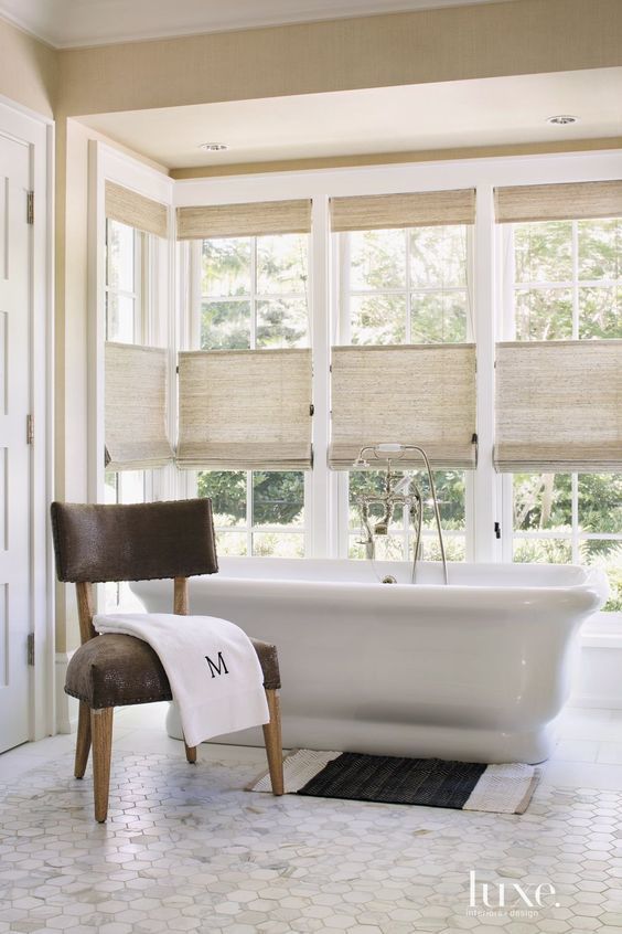 a white bath tub sitting next to a window with roman shades on it's windows