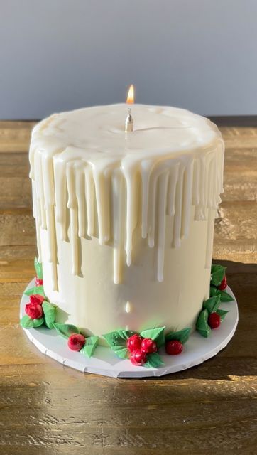 a white frosted cake sitting on top of a wooden table next to a lit candle