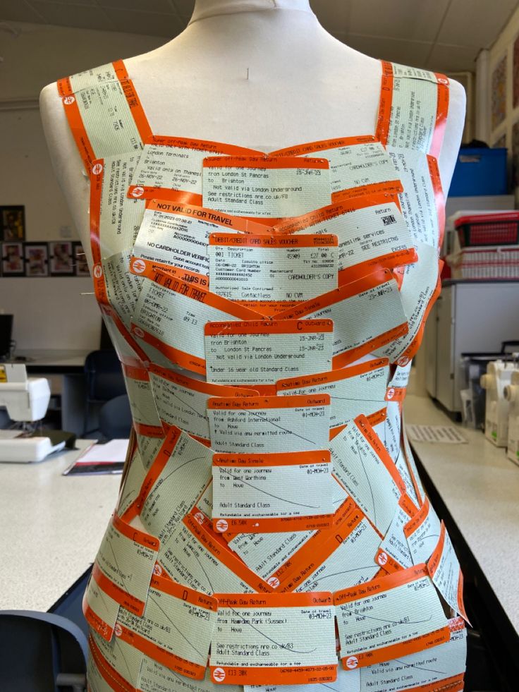 an orange and white dress made out of strips of paper on a mannequin