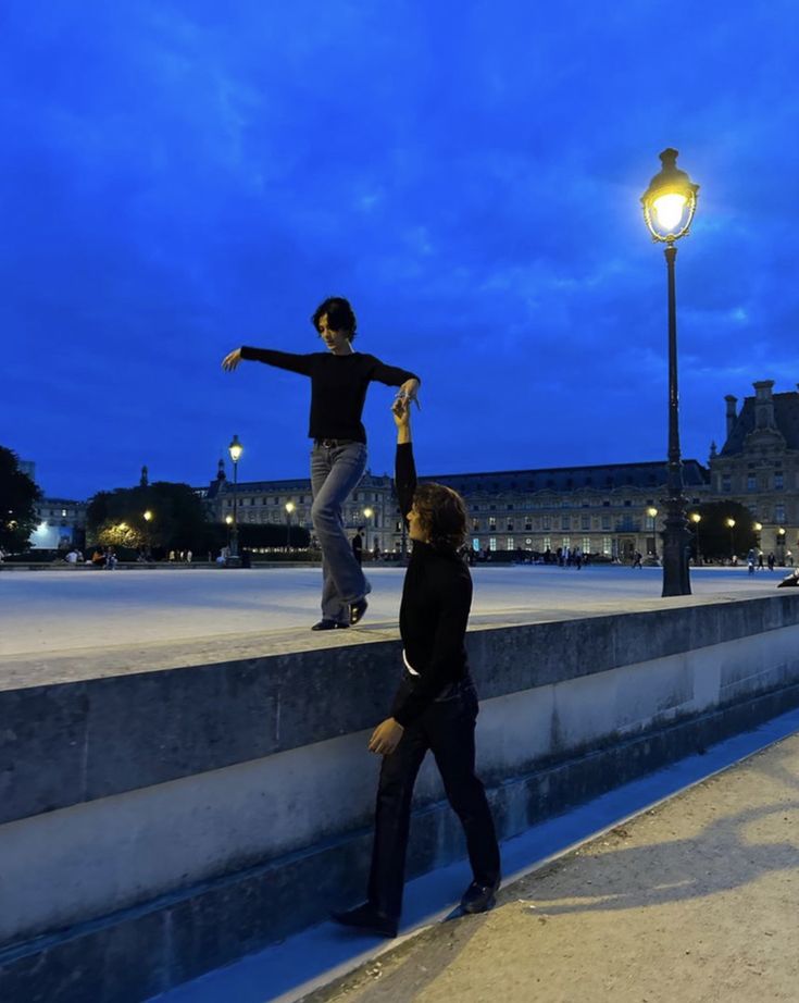 two people standing on the edge of a stone wall near a street light at night