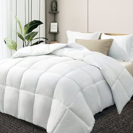 a white comforter on a bed with pillows and pillow cases in front of a window