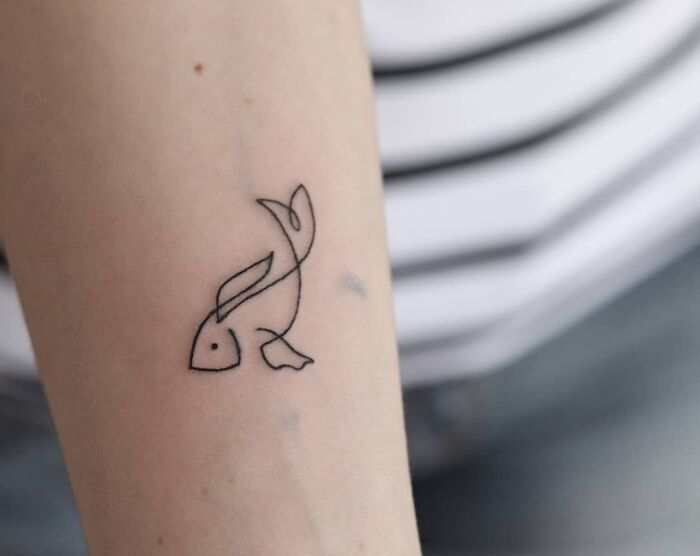 a small tattoo on the arm of a woman's left arm, depicting a fish