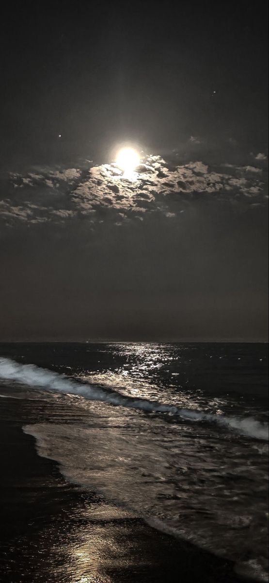 the moon shines brightly over the ocean on a dark night with waves coming in