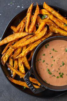 french fries with dipping sauce on a black plate next to a bowl of ranch dressing