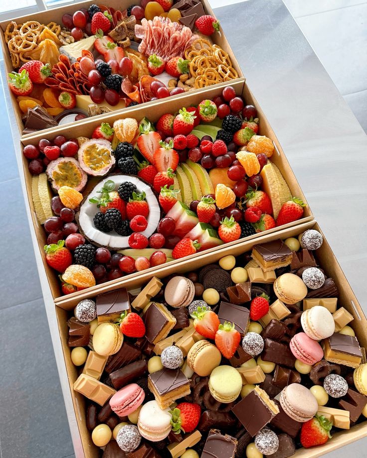 two trays filled with assorted fruit and sweets on top of a white table