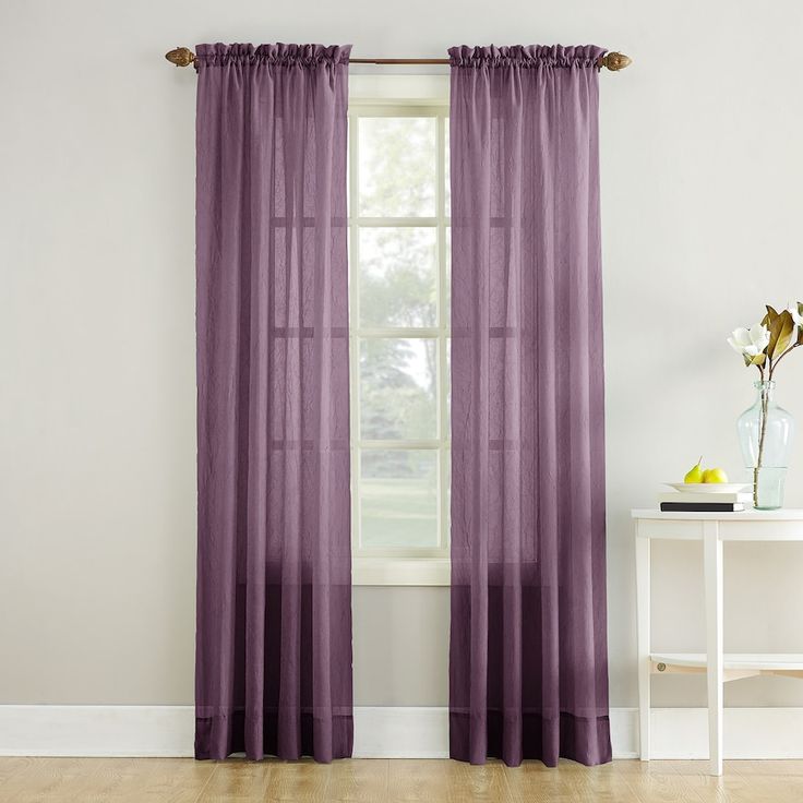 a purple curtain hanging in front of a window with a white table and vase on it