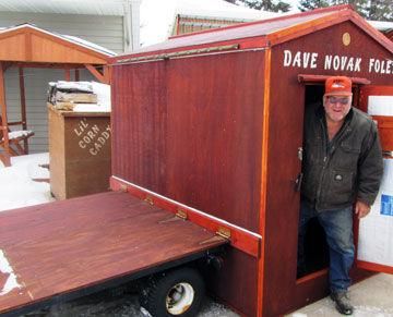 a man standing in the doorway of a small wooden building with snow on the ground