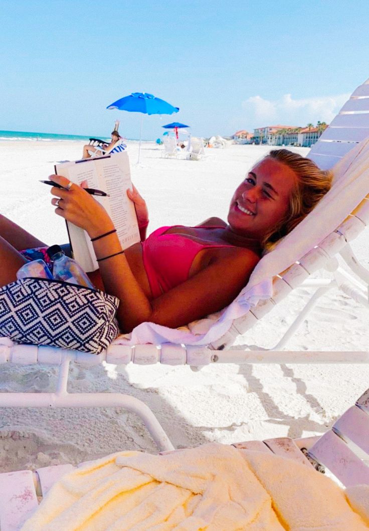 a woman laying in a hammock on the beach reading a book and smiling