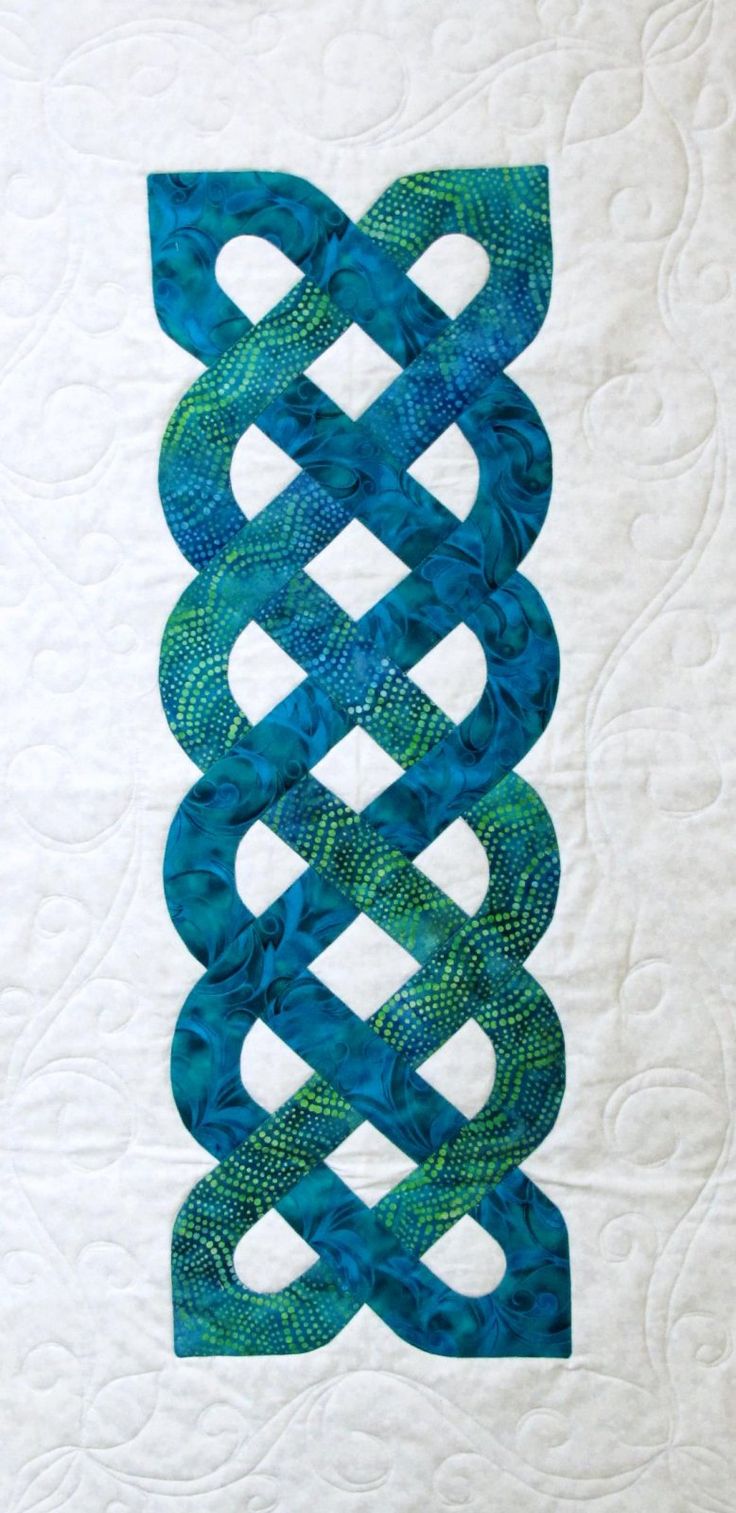 a quilted wall hanging on the side of a white wall with blue and green designs