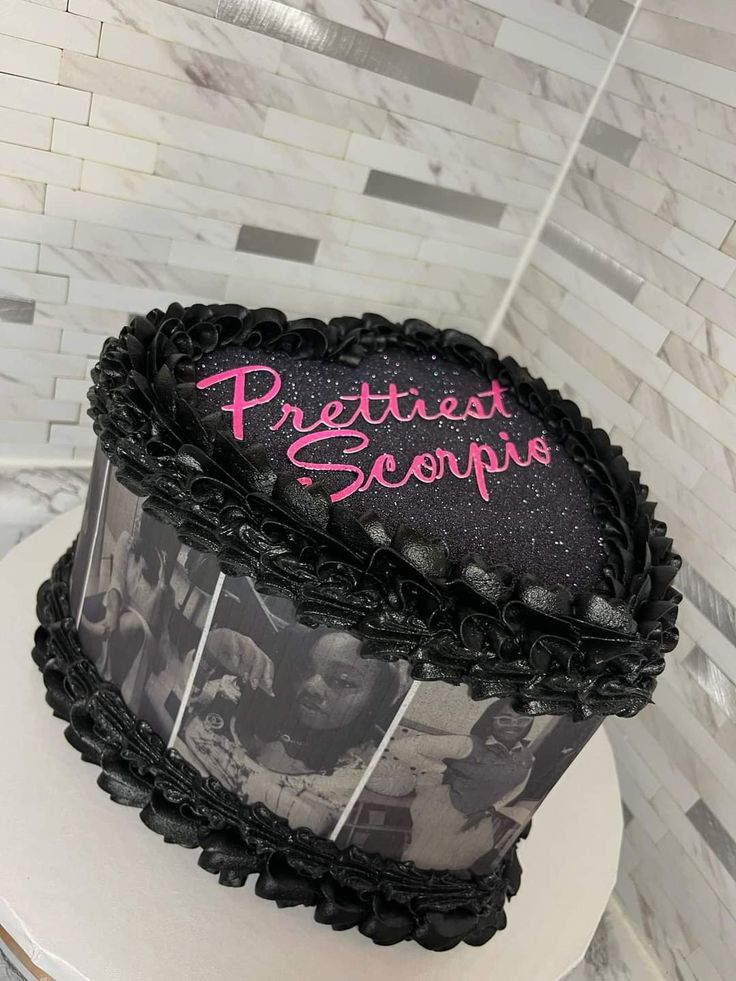 a black and white cake with pink writing on it sitting on a pedestal in front of a tiled wall