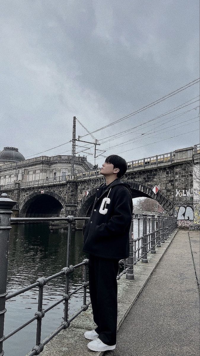 a man standing on the side of a river next to a bridge