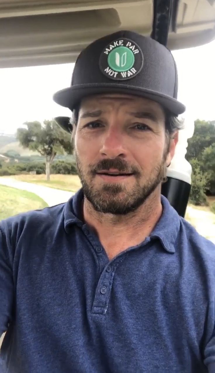 a man wearing a black hat while sitting in a golf cart on a sunny day