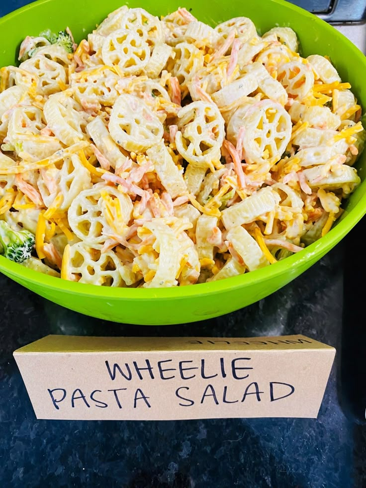 a green bowl filled with pasta salad next to a sign that says wheelie pasta salad