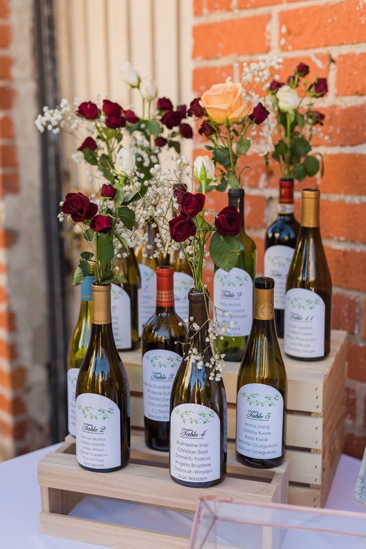 wine bottles are lined up on a table with flowers in vases and labels for each bottle