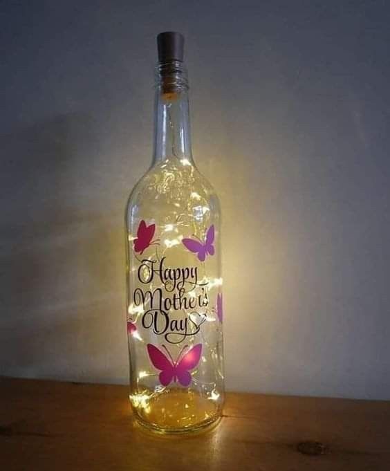 a bottle that is sitting on a table with some lights in it and the words happy mother's day written on it