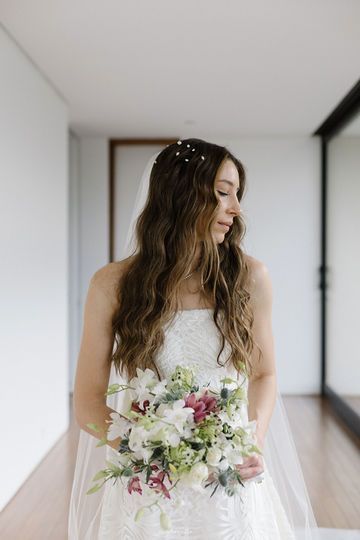 a woman in a wedding dress holding a bouquet and looking down at her face while standing on a hard wood floor