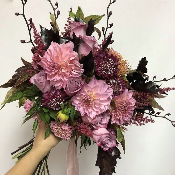 a bouquet of flowers is being held by a woman's hand with pink ribbon