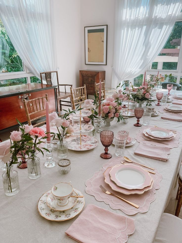 the table is set with pink and white plates, place settings, and vases