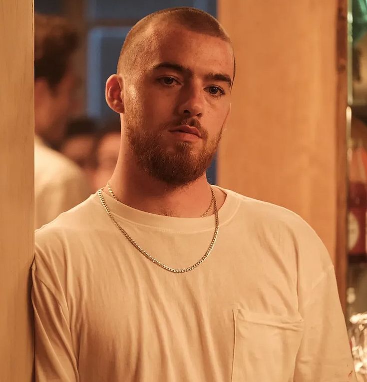 a man standing next to a wall with a chain on it's neck and wearing a white t - shirt