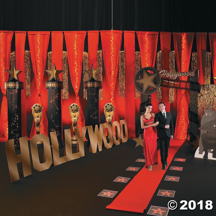 a man and woman walking down a red carpeted hallway in front of hollywood decorations