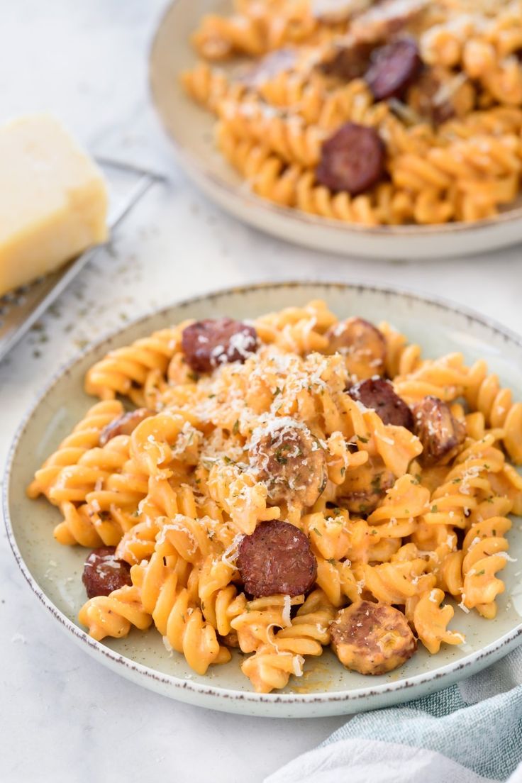 two plates of pasta with sausage and parmesan cheese on the table next to butter