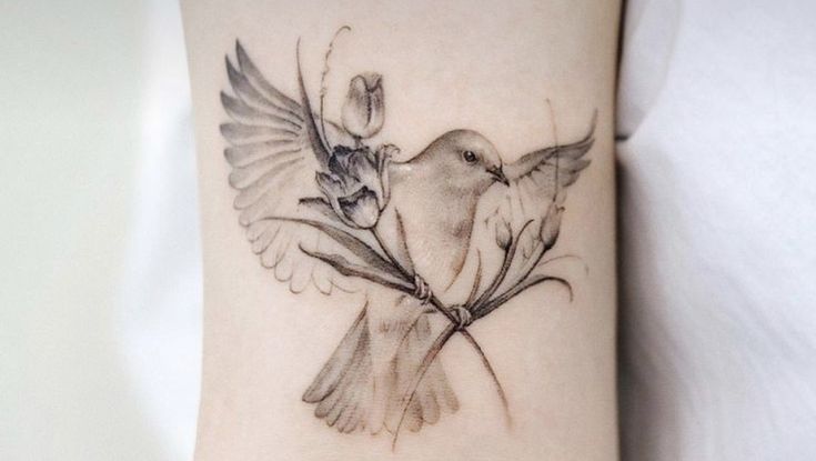 a tattoo with a bird and flowers on the wrist is shown in black and white