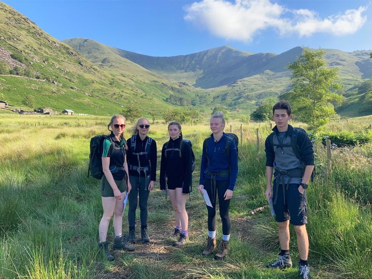 four people standing in the grass with mountains in the background