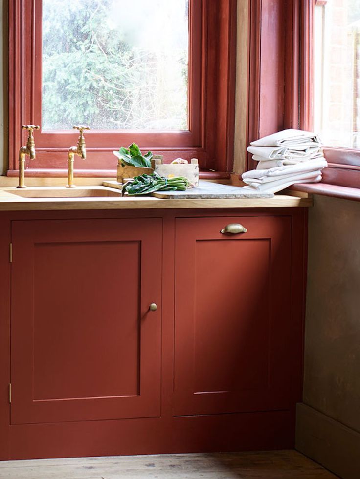 a kitchen with red painted cabinets and a sink in front of a window filled with papers