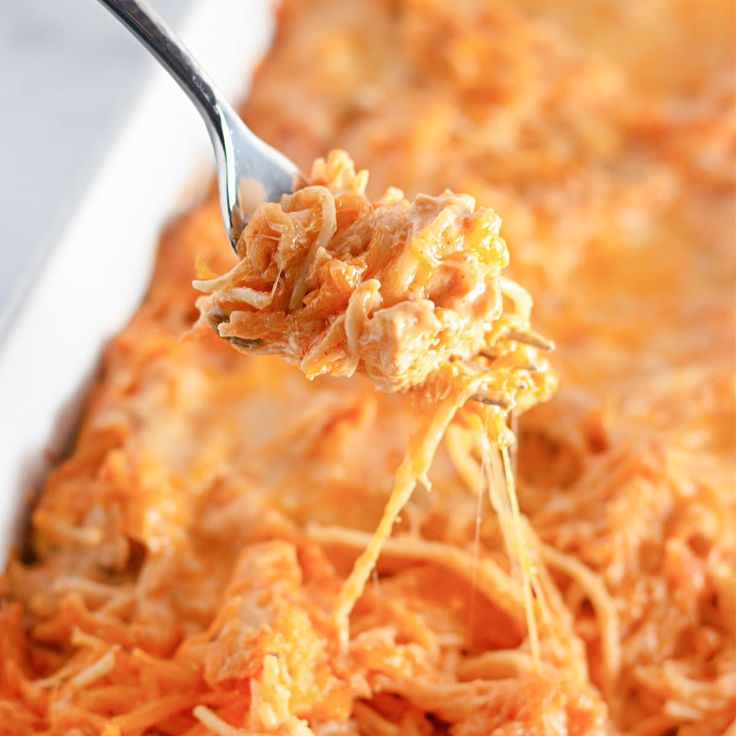 a spoon full of shredded cheese being lifted from a casserole dish