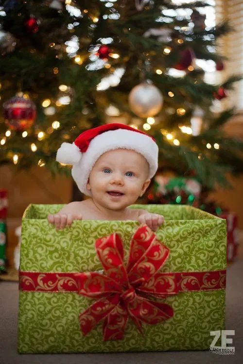 a baby wearing a santa hat sitting in front of a christmas tree holding a present