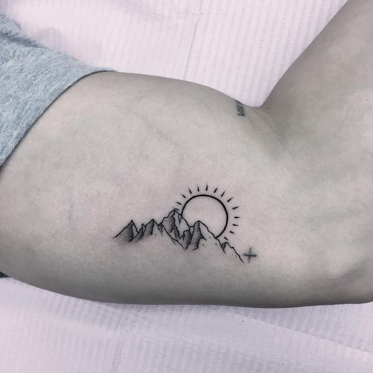 a person's arm with a small tattoo on it, and the sun in the background