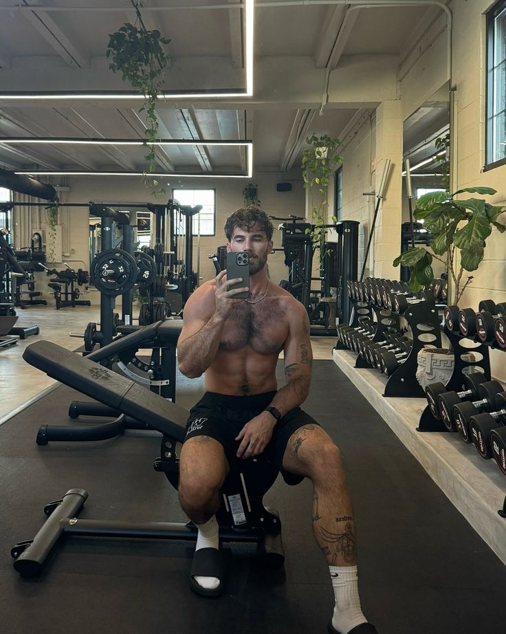 a man taking a selfie while sitting on a bench in a gym with his cell phone