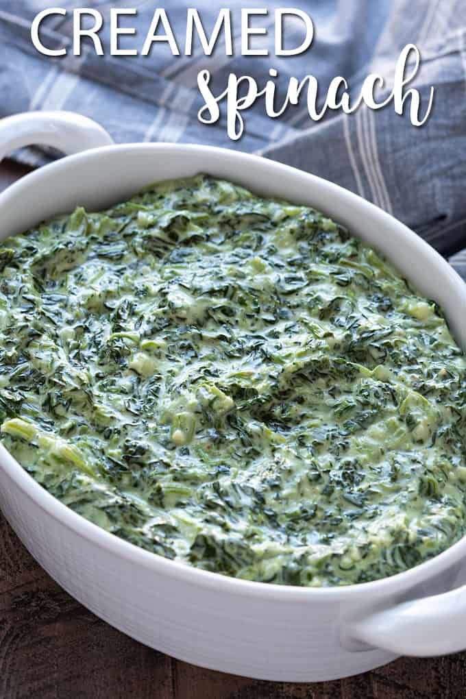 a white bowl filled with spinach on top of a wooden table next to a napkin