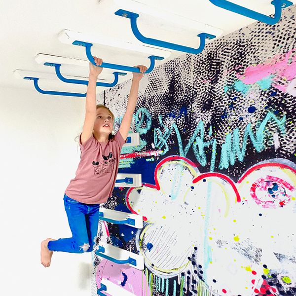 a young boy climbing up the side of a graffiti covered wall with his arms in the air