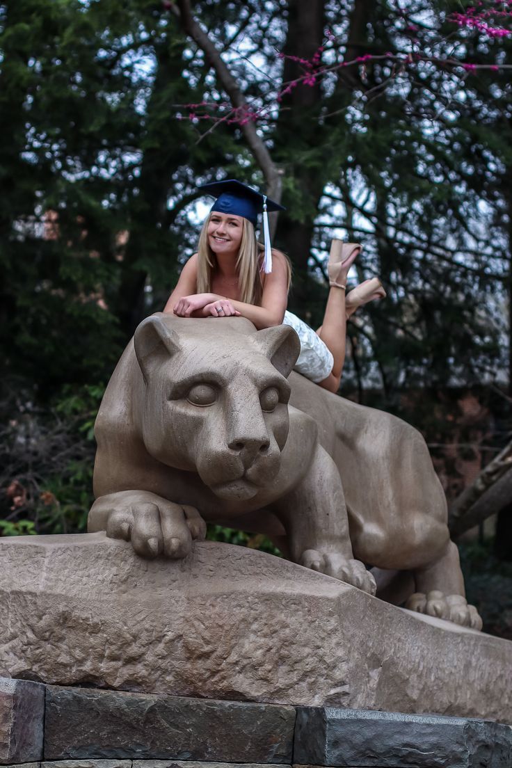 a woman sitting on top of a statue of a lion in front of some trees