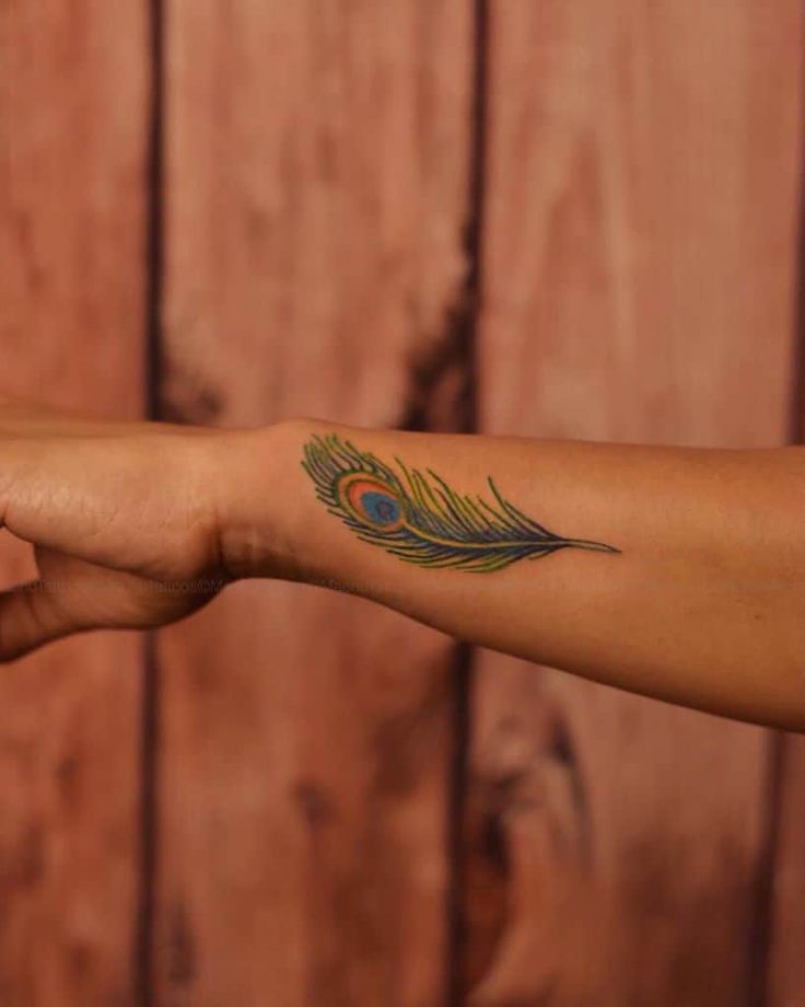 a woman's arm with a peacock feather tattoo on the left side of her arm