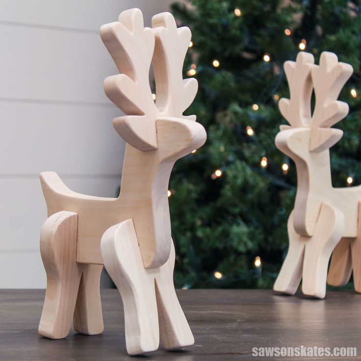 two wooden reindeer figurines sitting on top of a table next to a christmas tree