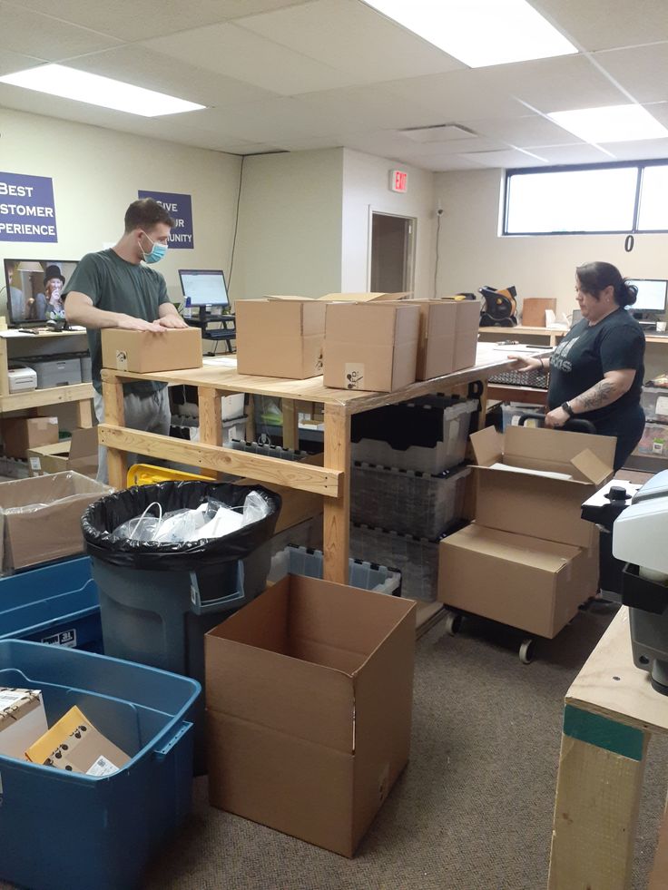 two people are working in an office with boxes on the floor