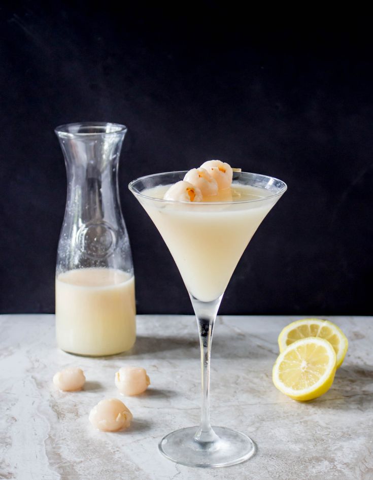 a drink in a glass next to a pitcher and lemon wedges