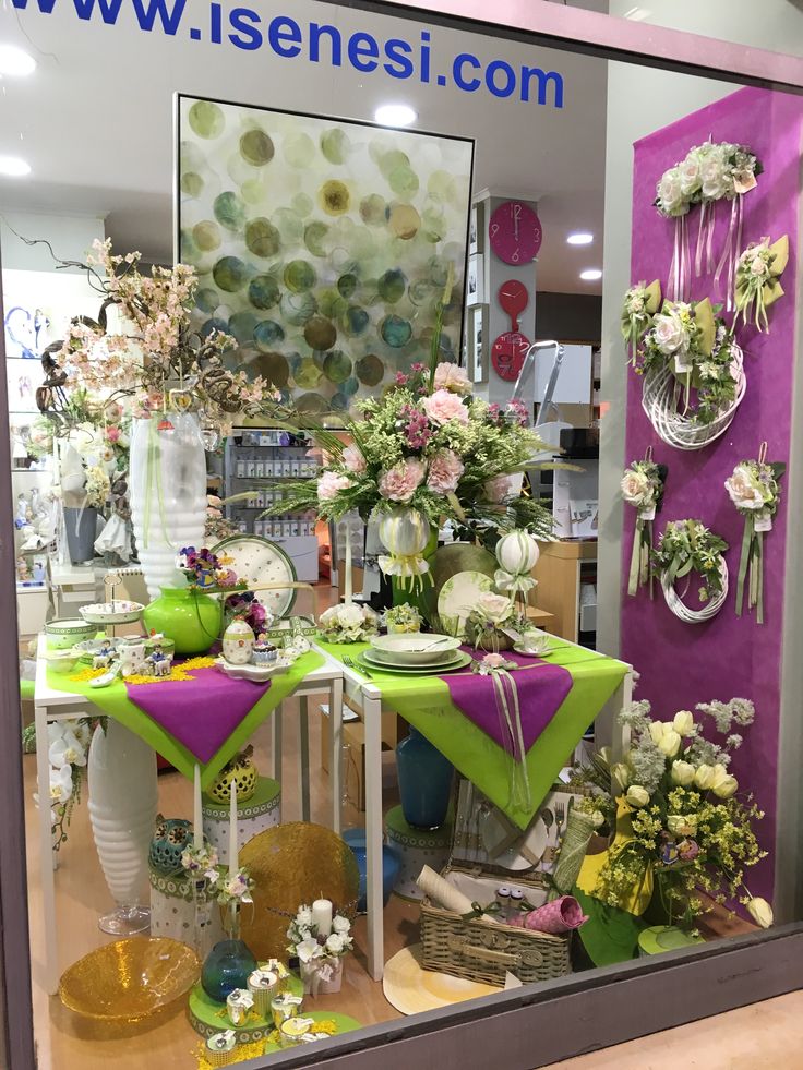 a window display with flowers and vases in the front, behind which is a green table cloth