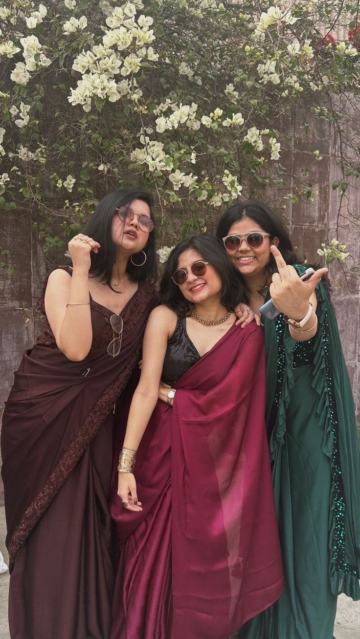 three women pose for the camera in front of a tree with white flowers on it