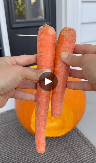 two carrots being held in front of a pumpkin