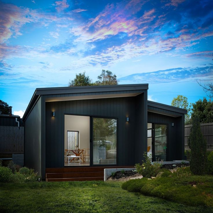 a small black house sitting on top of a lush green field under a blue sky