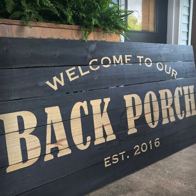 a welcome to our back porch sign on the side of a house with potted plants