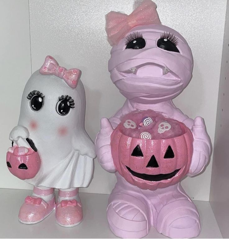 two halloween figurines sitting on top of a white shelf next to each other