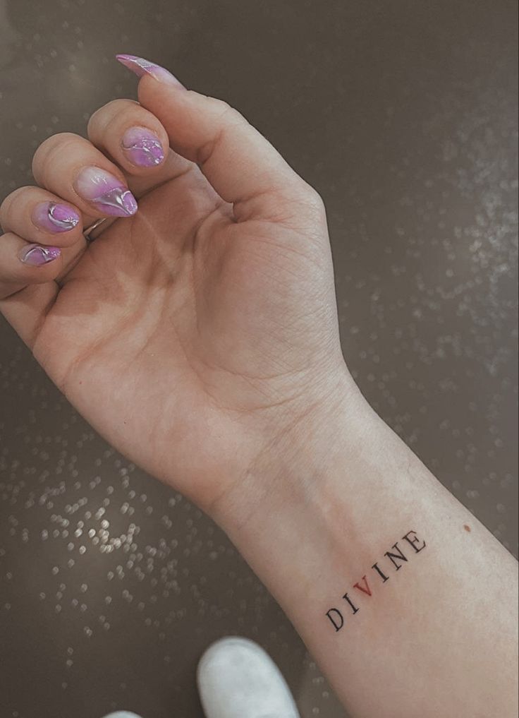 a woman's hand with a small tattoo on it that says divine above her left wrist