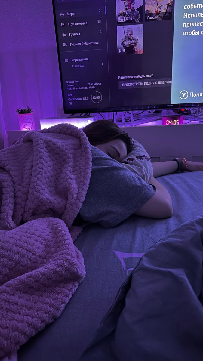 a person laying on a bed in front of a flat screen tv with purple lighting